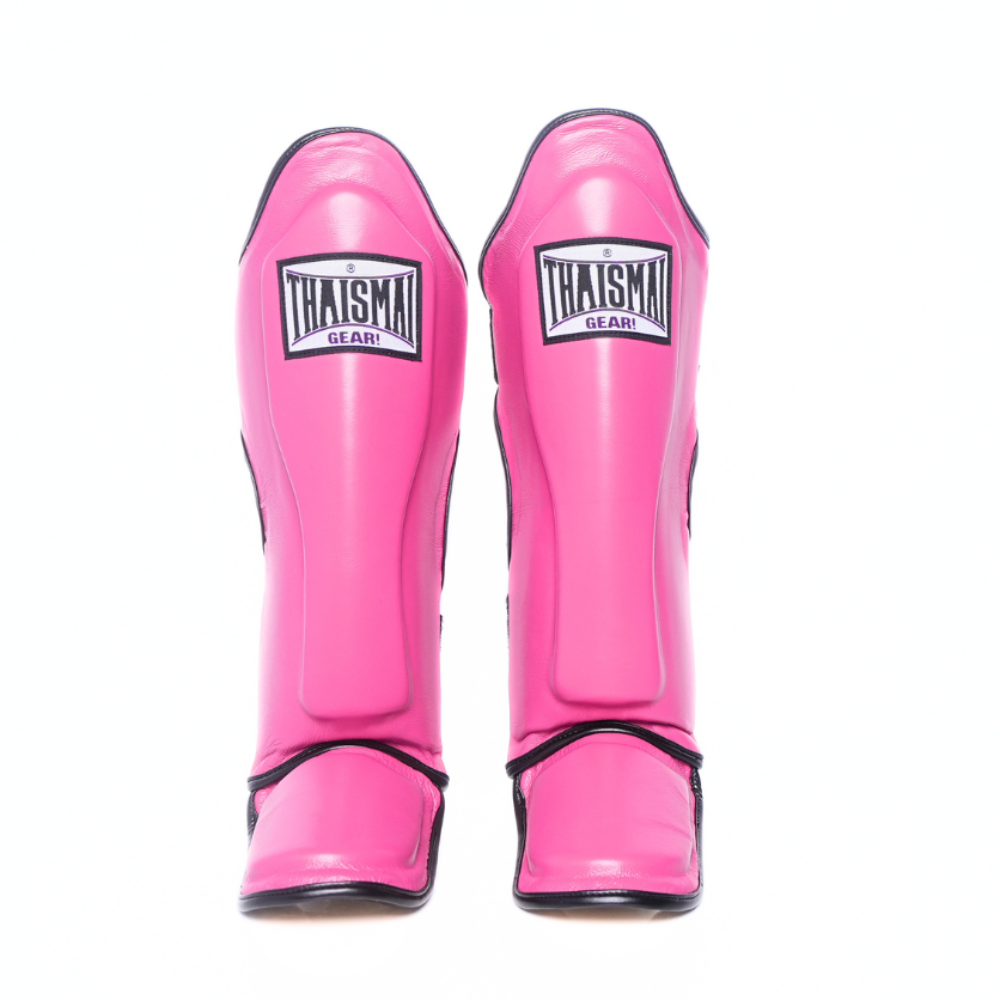 A pair of bright pink shin guards with black trim and a white and black 'THAISMAN' logo patch on the front, shown against a plain white background.