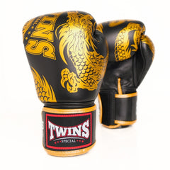 A pair of black boxing gloves with gold dragon graphics and a black wrist strap featuring a red and white 'TWINS SPECIAL' logo, set against a plain white background.